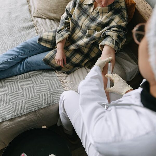 A healthcare professional carefully administers an injection to a patient sitting on a sofa in a cozy room.