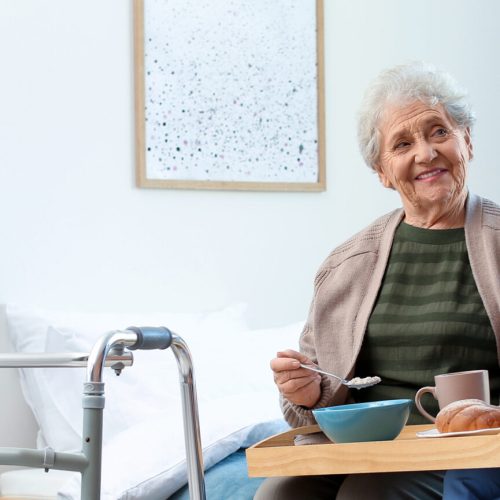 Care,Worker,Serving,Dinner,For,Elderly,Woman,On,Geriatric,Hospice.